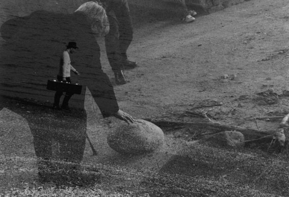 奄美大島、網野子集落のイビガナシ（丸石）に触れる山口昌男。その体の影の彼方、伊須集落の浜を永良部三絃を持って歩く今福龍太。二重露光撮影は濱田康作。2003年12月24日。